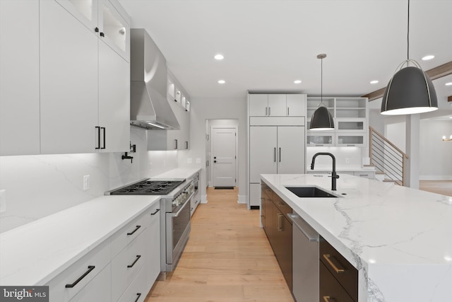 kitchen with wall chimney exhaust hood, hanging light fixtures, high quality appliances, white cabinets, and light wood-type flooring