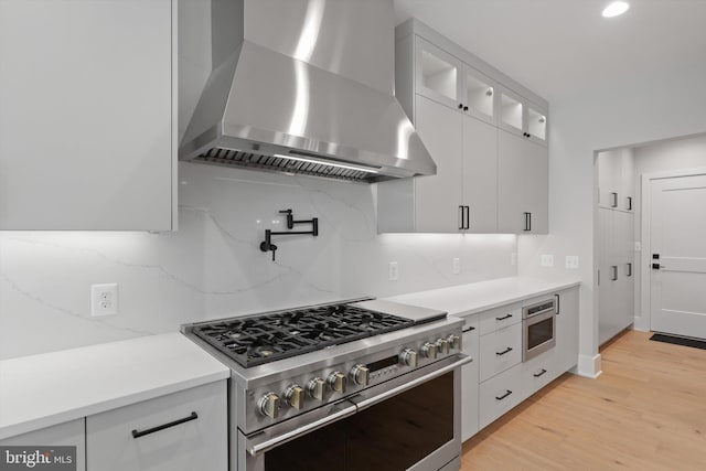 kitchen with white cabinetry, stainless steel appliances, wall chimney range hood, backsplash, and light wood-type flooring