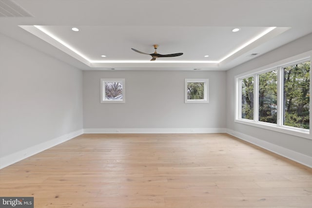 unfurnished room featuring a tray ceiling, ceiling fan, and light hardwood / wood-style floors