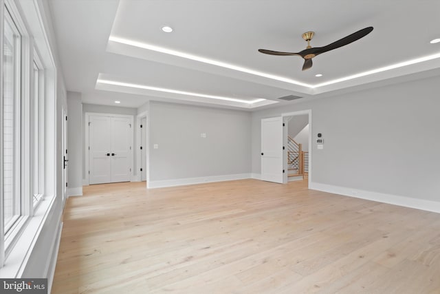 empty room with ceiling fan, a raised ceiling, and light hardwood / wood-style flooring