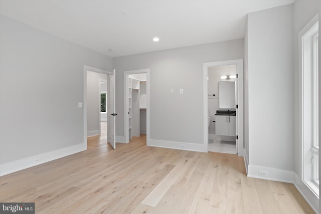 unfurnished bedroom featuring a closet, a walk in closet, ensuite bathroom, and light hardwood / wood-style flooring