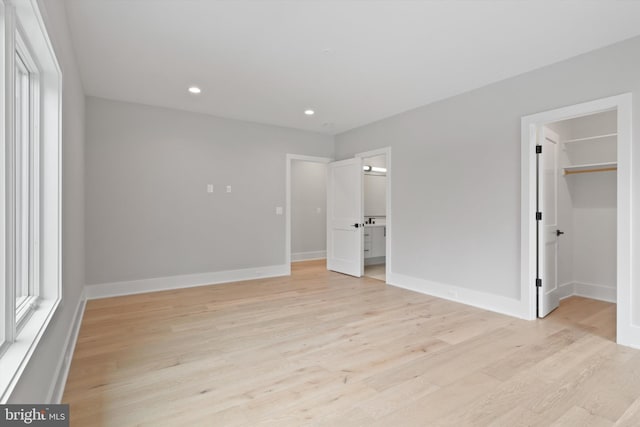 unfurnished bedroom with light wood-type flooring, a walk in closet, and a closet