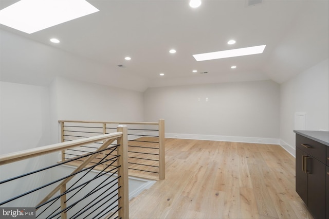 interior space featuring lofted ceiling with skylight and light hardwood / wood-style flooring