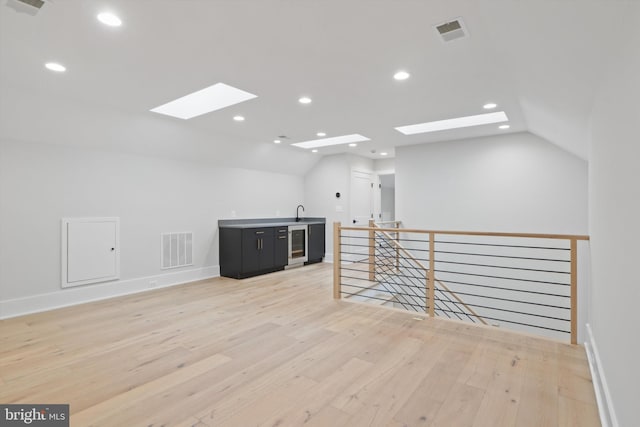 additional living space featuring wine cooler, light hardwood / wood-style floors, and lofted ceiling with skylight