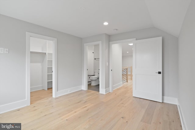 unfurnished bedroom featuring ensuite bath, vaulted ceiling, a spacious closet, light hardwood / wood-style floors, and a closet