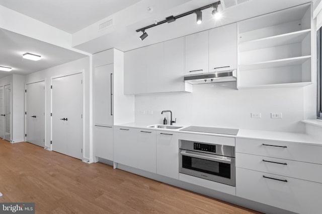 kitchen featuring black electric stovetop, stainless steel oven, sink, light hardwood / wood-style flooring, and white cabinets