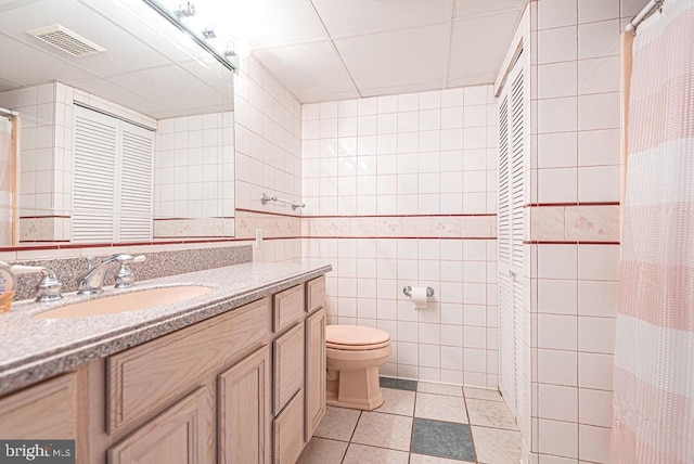 bathroom with curtained shower, tile patterned floors, toilet, vanity, and tile walls