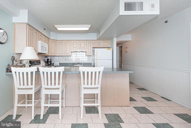 kitchen with decorative backsplash, a kitchen breakfast bar, kitchen peninsula, white appliances, and light brown cabinets