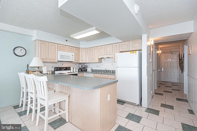 kitchen featuring white appliances, sink, tasteful backsplash, a kitchen bar, and kitchen peninsula