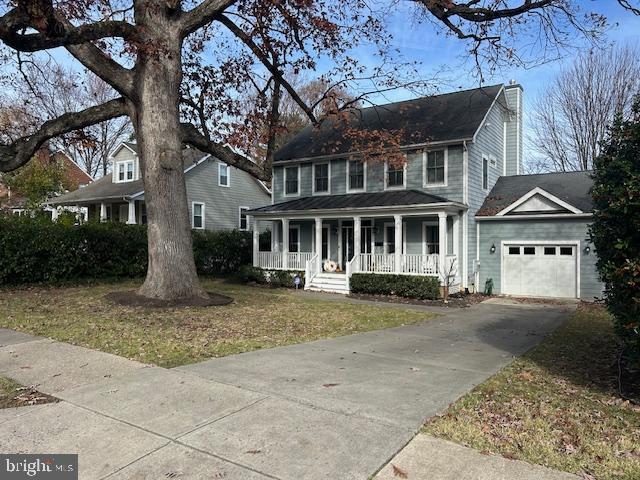 colonial-style house with a garage, covered porch, an outbuilding, and a front yard