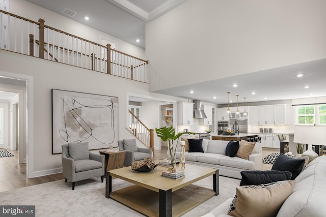 living room featuring light wood-type flooring, sink, a towering ceiling, and ornamental molding