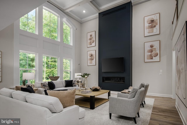 living room with a wealth of natural light, a towering ceiling, ornamental molding, and hardwood / wood-style flooring