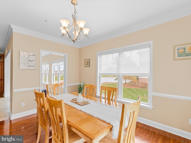 dining space with wood-type flooring, ornamental molding, and an inviting chandelier