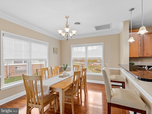 dining area featuring a chandelier, light wood-type flooring, crown molding, and a healthy amount of sunlight