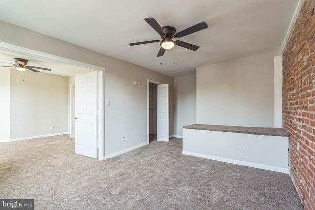 carpeted empty room featuring ceiling fan and brick wall