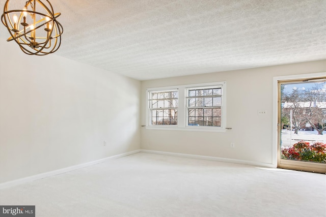 carpeted spare room with a textured ceiling and a chandelier