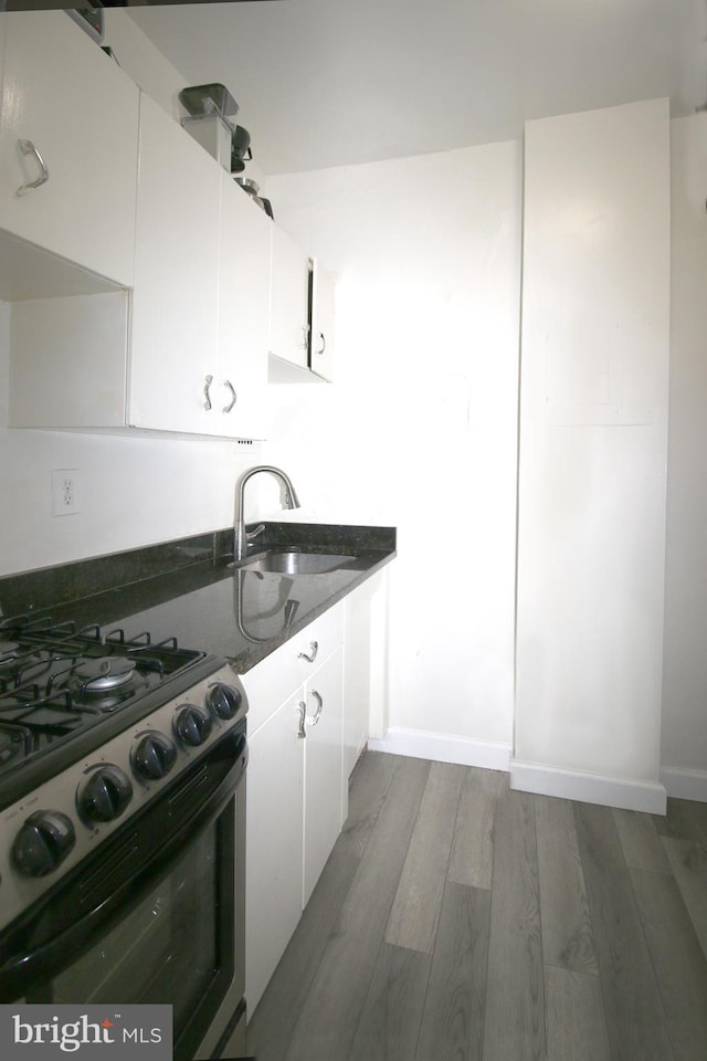 kitchen with stove, white cabinets, hardwood / wood-style floors, and sink