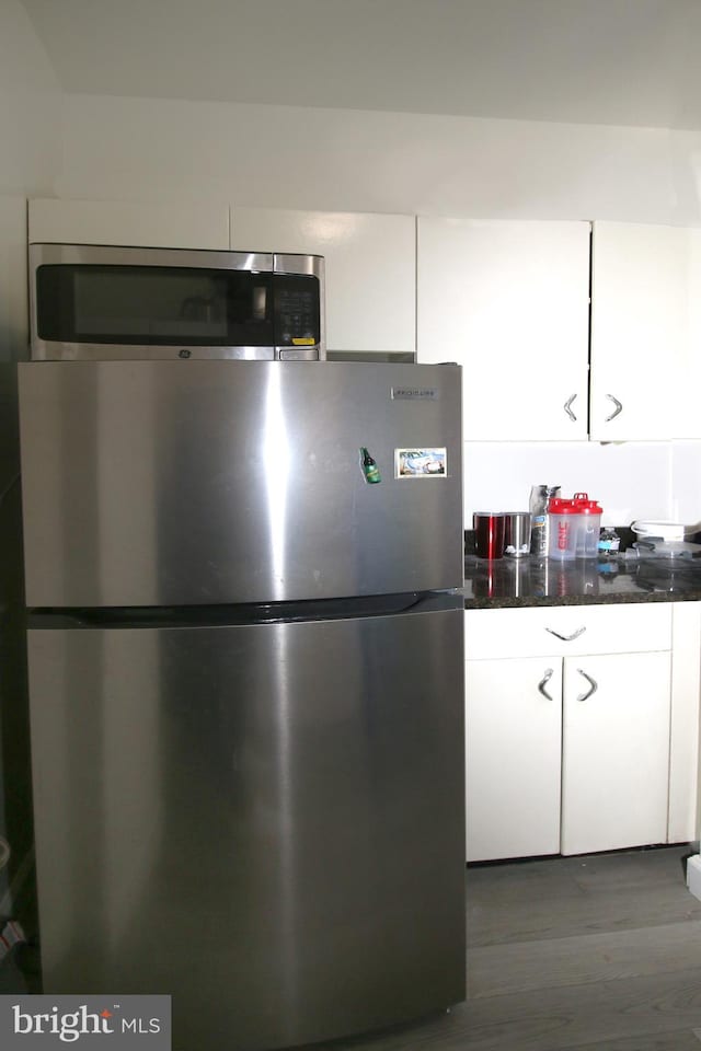 kitchen with white cabinets, stainless steel appliances, dark hardwood / wood-style floors, and dark stone counters