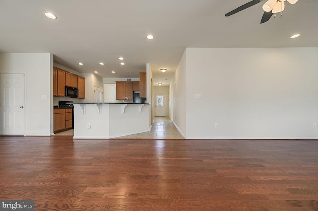 kitchen featuring hardwood / wood-style flooring, a breakfast bar area, black appliances, and ceiling fan