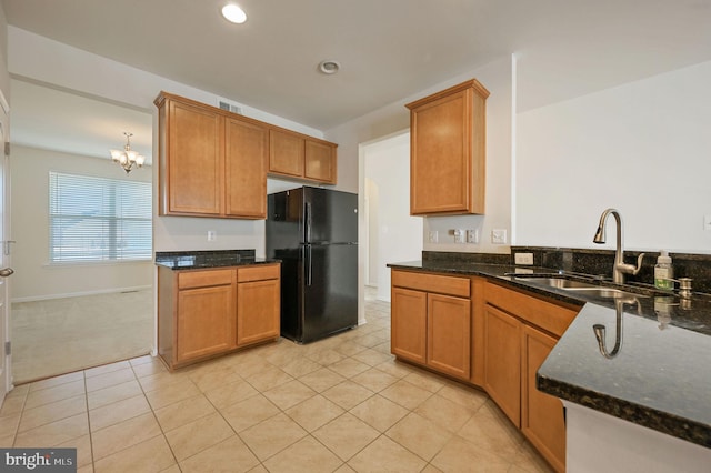 kitchen with light tile patterned flooring, sink, black fridge, a chandelier, and dark stone counters