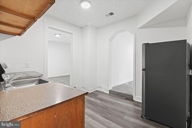 kitchen featuring hardwood / wood-style floors, sink, stainless steel refrigerator, and a textured ceiling