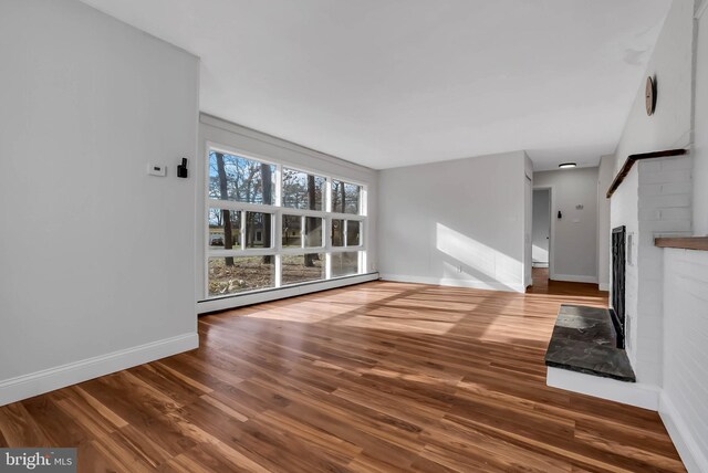 unfurnished living room with hardwood / wood-style floors, a brick fireplace, and a baseboard heating unit