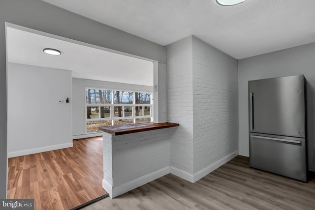 kitchen with a baseboard radiator, kitchen peninsula, stainless steel fridge, hardwood / wood-style floors, and a textured ceiling