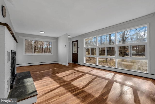 unfurnished living room featuring a healthy amount of sunlight, wood-type flooring, and a baseboard radiator