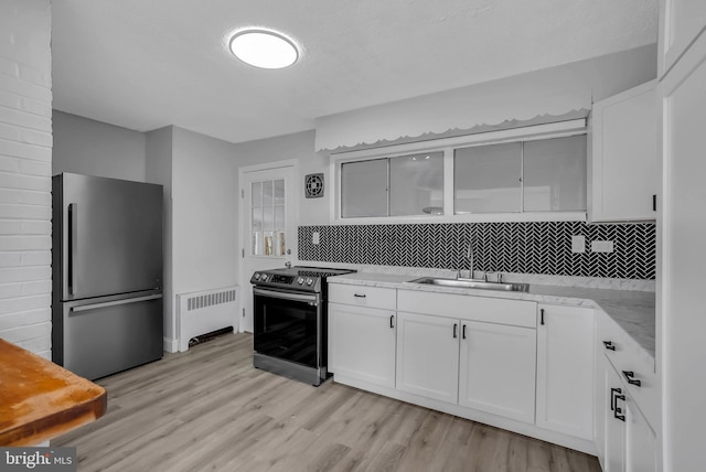 kitchen with radiator, white cabinets, sink, light wood-type flooring, and stainless steel appliances