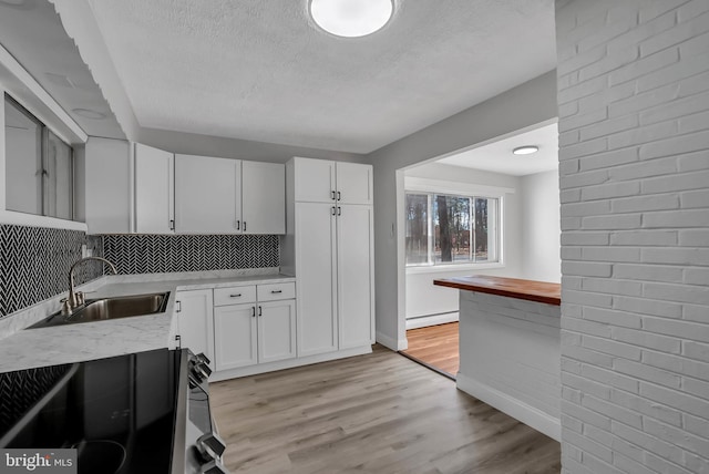 kitchen featuring white cabinetry, sink, black stove, baseboard heating, and light wood-type flooring