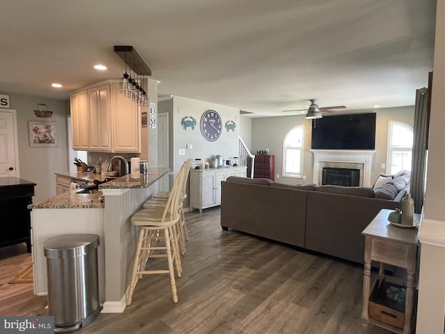 kitchen with a kitchen breakfast bar, sink, dark hardwood / wood-style floors, light stone counters, and kitchen peninsula