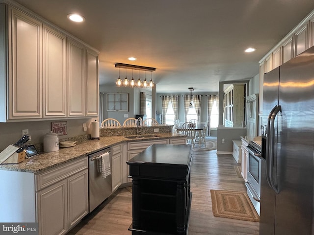 kitchen featuring kitchen peninsula, appliances with stainless steel finishes, sink, decorative light fixtures, and light hardwood / wood-style flooring