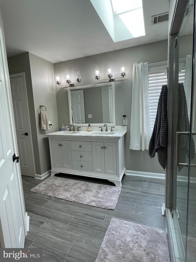 bathroom featuring wood-type flooring, vanity, a skylight, and a shower with shower door