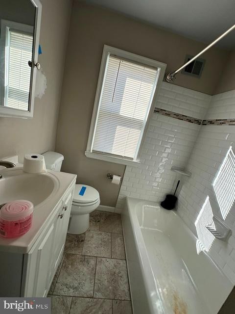 full bathroom with tiled shower / bath, vanity, toilet, and plenty of natural light