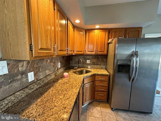 kitchen featuring sink, stainless steel refrigerator with ice dispenser, decorative backsplash, light tile patterned floors, and light stone counters