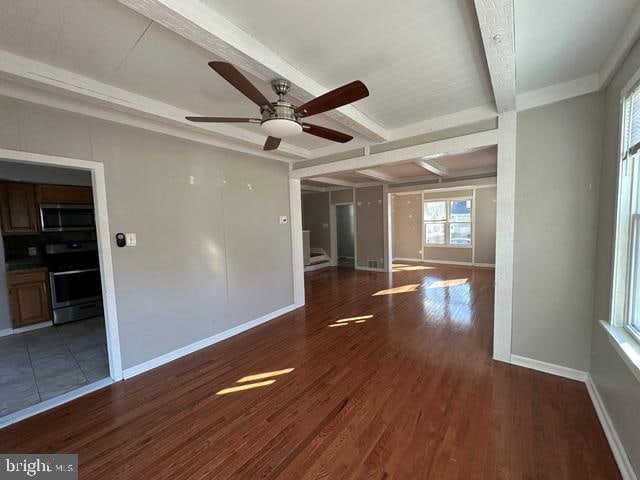 empty room with beam ceiling, ceiling fan, and dark wood-type flooring