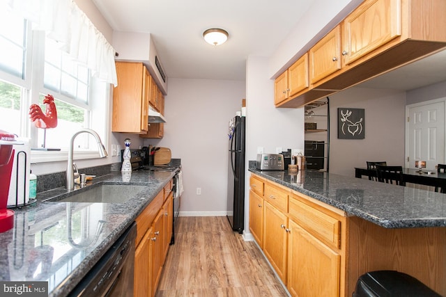 kitchen with sink, light hardwood / wood-style flooring, kitchen peninsula, dark stone countertops, and black appliances