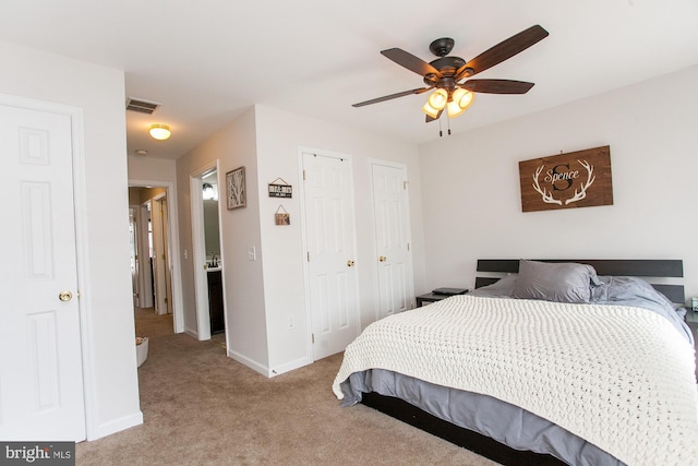 bedroom with light colored carpet, ceiling fan, and multiple closets