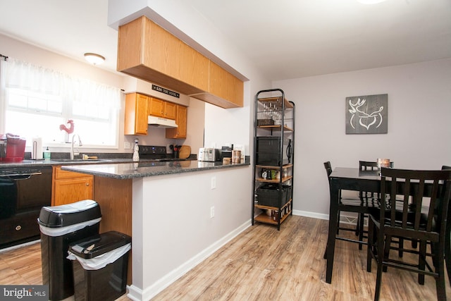 kitchen featuring sink, kitchen peninsula, dark stone countertops, black appliances, and light wood-type flooring