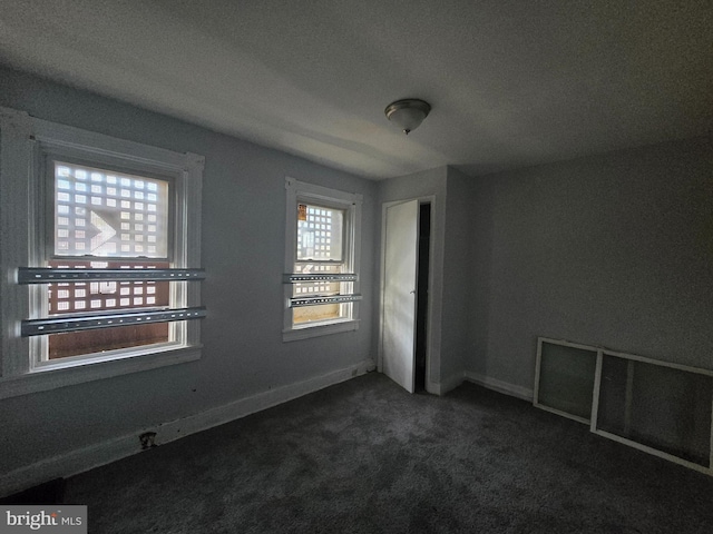 spare room featuring dark carpet and a textured ceiling