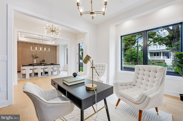 living area with a raised ceiling, a chandelier, a healthy amount of sunlight, and light hardwood / wood-style floors