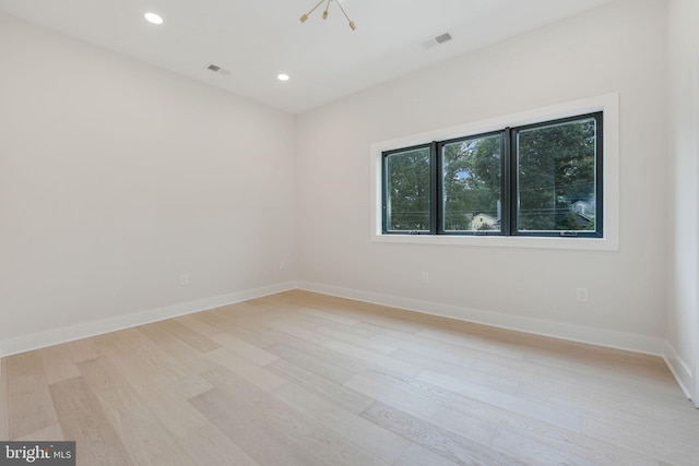 spare room featuring a chandelier and light hardwood / wood-style flooring