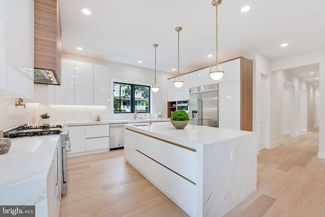 kitchen with white cabinetry, hanging light fixtures, stainless steel appliances, light stone counters, and a kitchen island