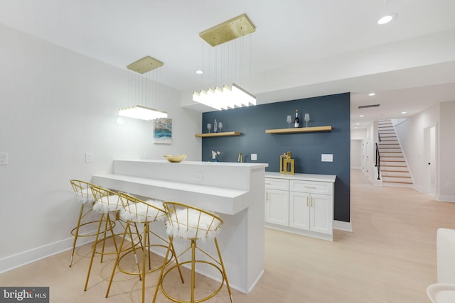 kitchen featuring pendant lighting, light hardwood / wood-style flooring, white cabinetry, kitchen peninsula, and a breakfast bar area