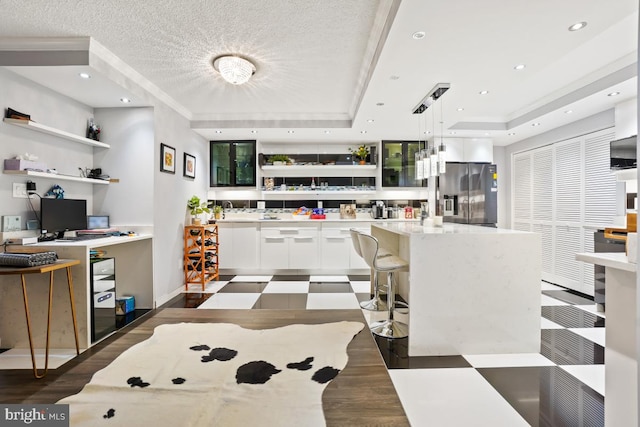 kitchen with a kitchen island, a raised ceiling, stainless steel refrigerator with ice dispenser, pendant lighting, and white cabinets