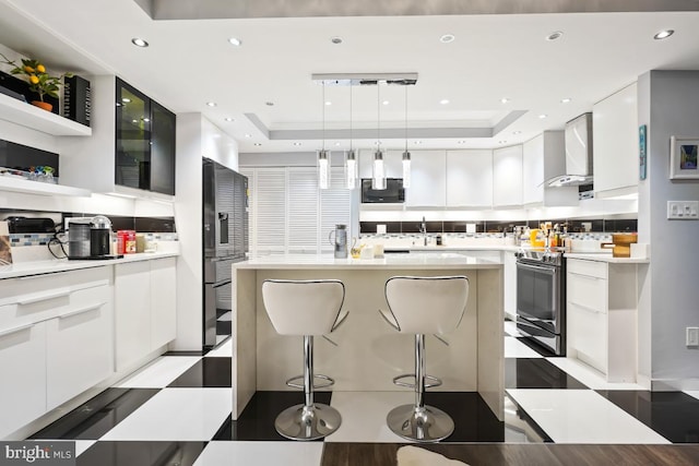 kitchen with white cabinets, a raised ceiling, stainless steel range with electric stovetop, and wall chimney range hood