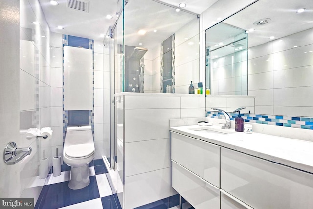 bathroom featuring vanity, decorative backsplash, toilet, tile walls, and a shower with shower door