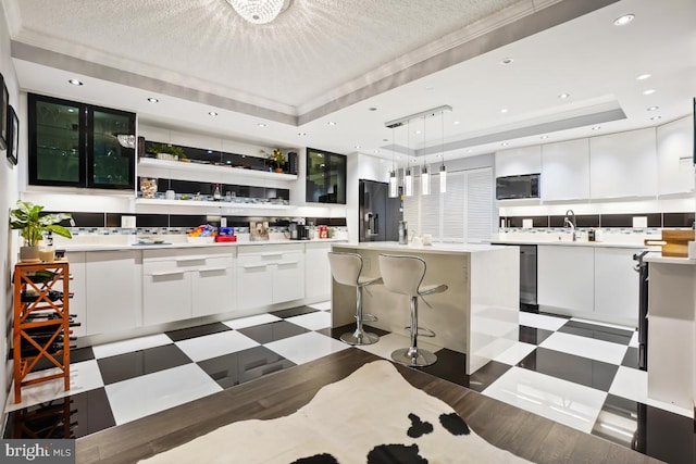 kitchen with a raised ceiling, a kitchen island, refrigerator with ice dispenser, pendant lighting, and white cabinetry