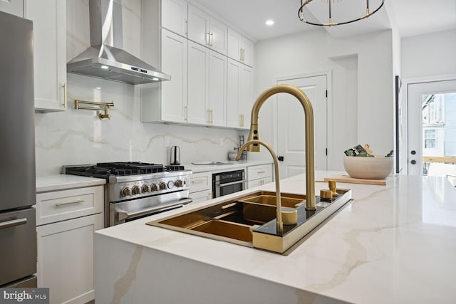 kitchen with light stone countertops, appliances with stainless steel finishes, backsplash, wall chimney exhaust hood, and white cabinetry