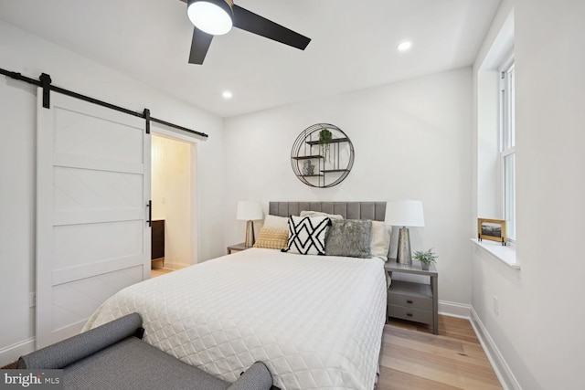 bedroom featuring ceiling fan, a barn door, and light hardwood / wood-style floors